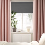 Chambre moderne avec des rideaux roses VILBORG, élégante, longue au sol, bloquant doucement la lumière. Plante en pot, lampe et radiateur blanc sous une grande fenêtre.