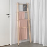 Le porte-serviettes en bois de bouleau contient des serviettes roses, à côté de la porte avec poignée argentée ; pochette grise au-dessus pour le stockage.