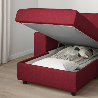 Canapé rouge avec pouf de rangement, couvercle ouvert laissant apparaître des couvertures pliées.