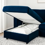 Un canapé-lit rembourré bleu avec rangements ; Le siège se souleva, révélant un matelas.