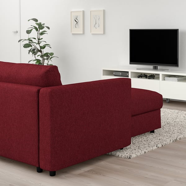Salon confortable avec grand canapé sectionnel VIMLE rouge contre mur blanc, télévision à écran plat sur pied, plante élégante et tapis.