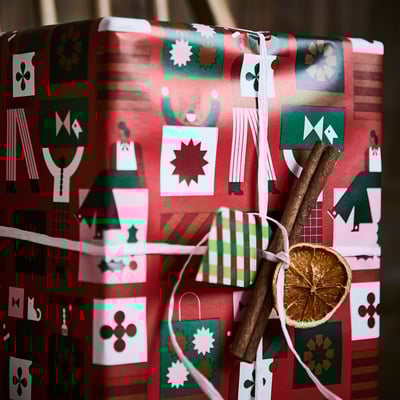 Papier cadeau rouge avec des motifs de Noël. Graphiques festifs en vert, blanc et marron sur fond rouge.