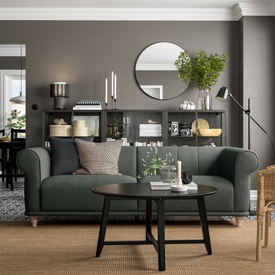 Salon moderne avec canapé vert VISKAFORS, table basse ronde noire, murs gris et décoration élégante.