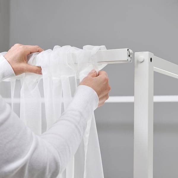 Personne ajustant des rideaux transparents blancs sur un cadre de lits à baldaquin VITARNA.