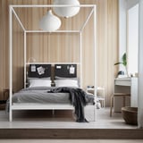Chambre moderne avec lit à baldaquin blanc VITARNA, draps gris, deux lampes sphériques, mur en panneaux de bois, commode blanche avec miroir, plante et lampe.