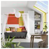 Lit gris moderne encadré de rideaux blancs, décoré d’oreillers colorés. Des œuvres d’art lumineuses, des étagères organisées et un bureau en bois avec une plante en pot.