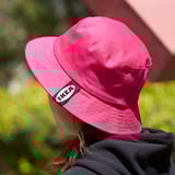 Woman wearing bright pink ikea bucket hat outdoors, shielding her face from the sun.