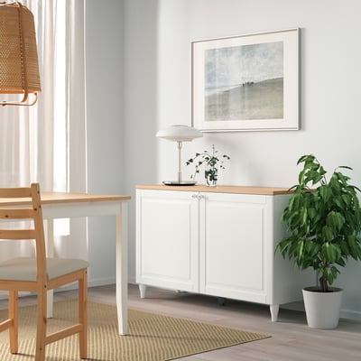 White BESTÅ sideboard with adjustable shelves between table & plant. Modern, minimalist design. Offers substantial storage.