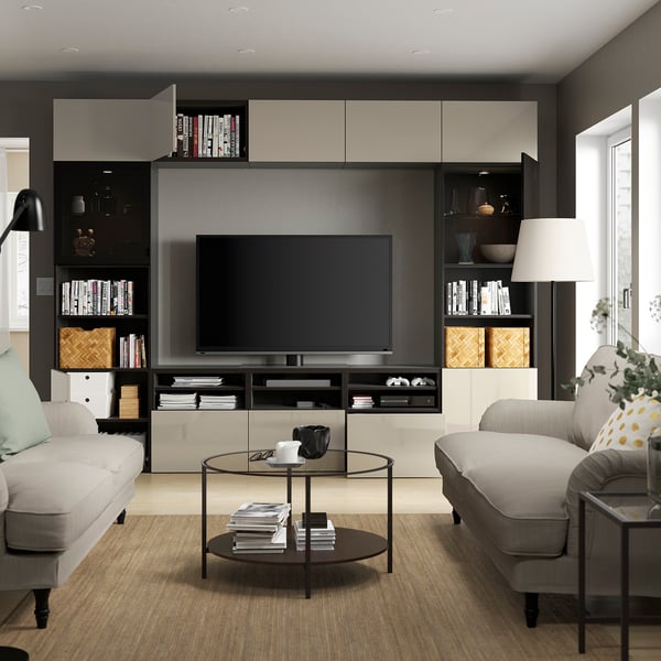 Modern living room with grey couches, circular glass coffee table, and large black tv on a stylish storage unit with shelves and cabinets.