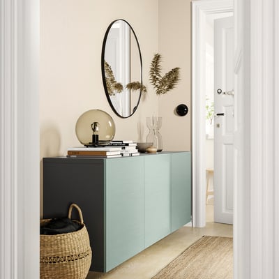Modern entryway with teal BESTÅ cabinet, round mirror, dried plants, books, and basket.