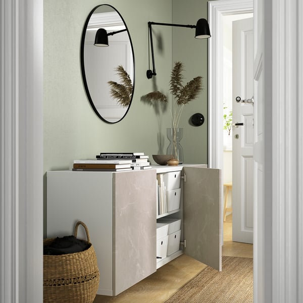 Wall-mounted BESTÅ unit with adjustable shelves and decorative knobs, mirror, and lamps beside doorway.