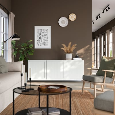 Modern living room with BESTÅ white cabinet, creating airy feel. Its large, housing books & plants, between windows & light fixtures.