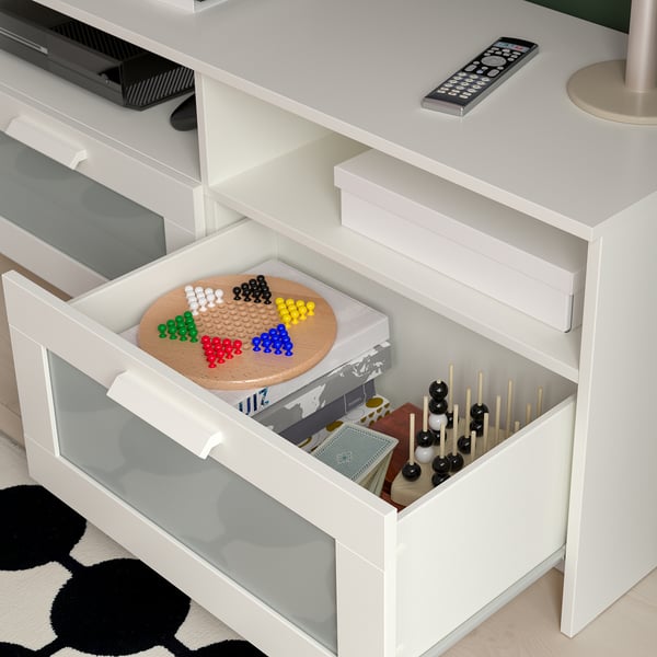 White tv bench with open drawer showing colourful beads, game pieces, remote on top.