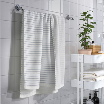 Modern bathroom with white tiles. BROKGINST towel, plants & toiletries. Natural light.
