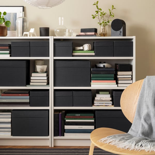 Modern living room with DRÖNA grey fabric storage boxes on shelves, blending neatly with books, creating organised & stylish space.