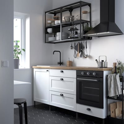 Modern white kitchen with black accents, featuring ENHET cabinets, a large cooktop, and open shelves with accessories.