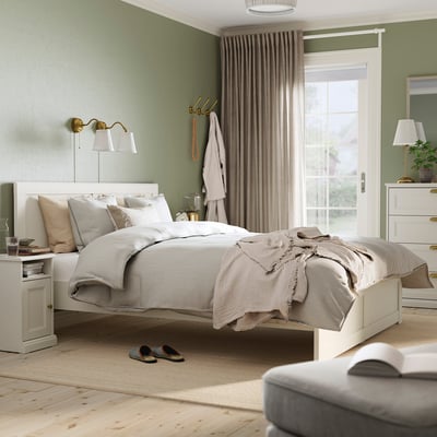 Cosy bedroom with white FÅGELFJÄLLET bed, striped sheets, beige throw, matching nightstands, and off-white chest.