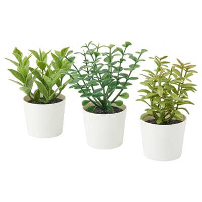Three white ceramic pots, each with green artificial plants, arranged in a row.