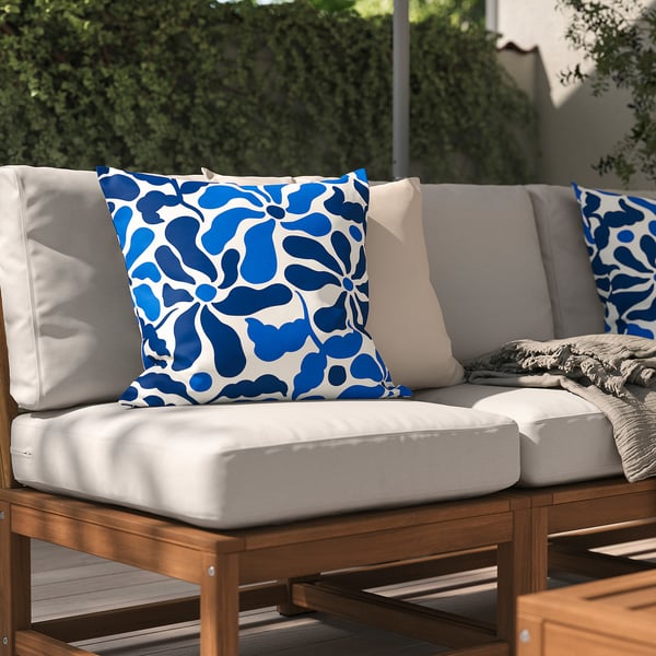 Outdoor grey sofa with blue patterned cushions, set against a green fence.