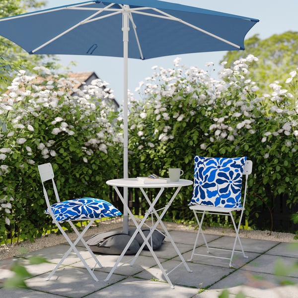 Charming outdoor patio set with blue cushions, round table, and large umbrella, ideal for garden relaxation.