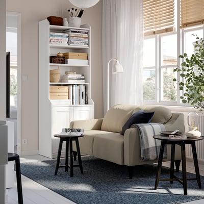 Modern living room with GULLVALLA sofa, bookshelf, side tables, and blue rug. Bright with natural light.