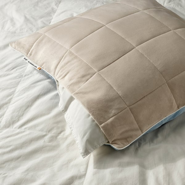 A beige pillow protector on a bed, featuring a cool blue side for warm nights and a warm beige side for cold nights.