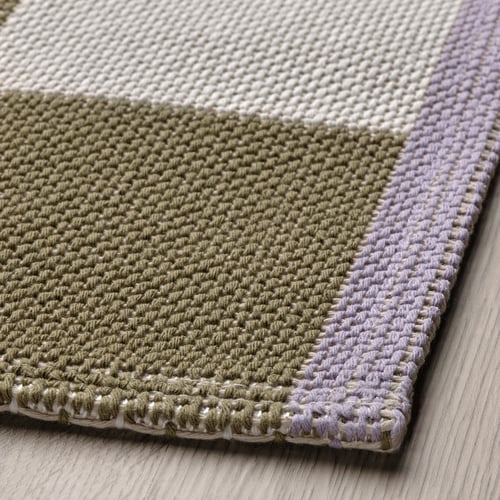 Textured, handwoven rug with subtle checkerboard pattern. Contrasting edges, laid on wood floor.