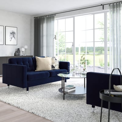 Modern living room with dark blue sofa, rug, coffee table, large windows, and black chair.