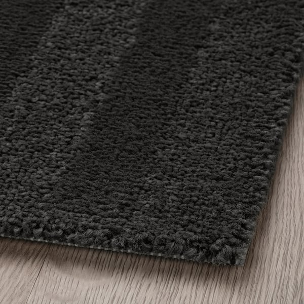 Close-up of soft, dark grey rug on wooden floor, showing texture and quality.