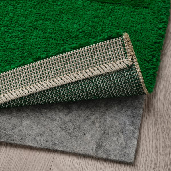 Green rug with anti-slip backing and folded edge for secure placement.