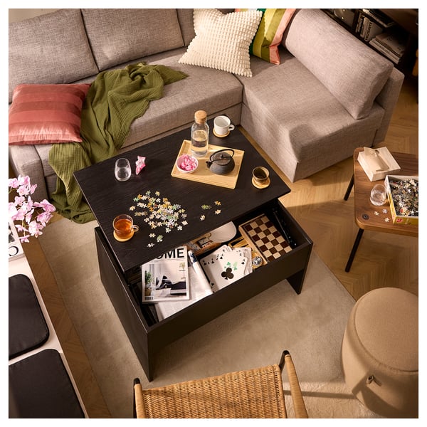 Grey couch, coffee table with teapot, open drawer with games, puzzle pieces, and flowers.