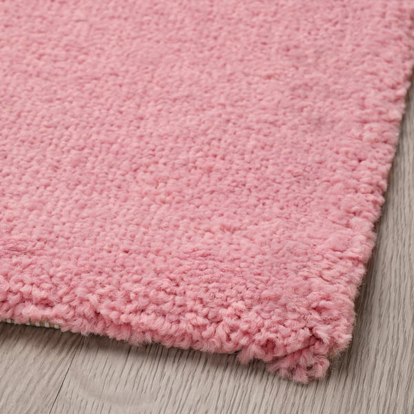 A closeup of a soft pink rug. Its curly yarns and texture are prominent, emphasising its cosy and high-quality feel.