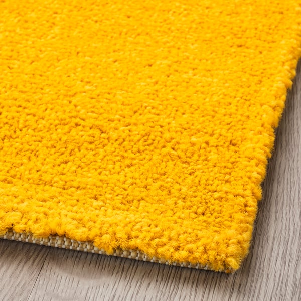 Close-up of soft, plush yellow rug on wooden floor, showcasing its high-quality texture and stitching.