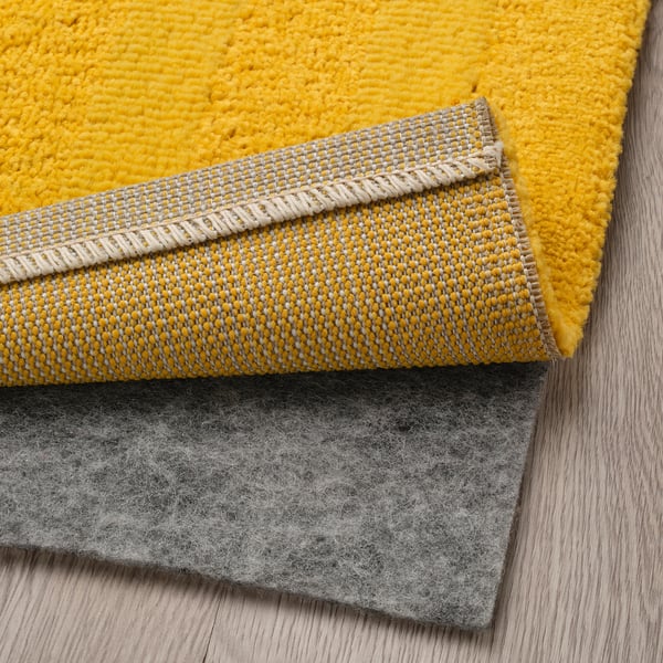 Yellow low pile rug with grey underside, displaying soft texture and anti-slip feature.