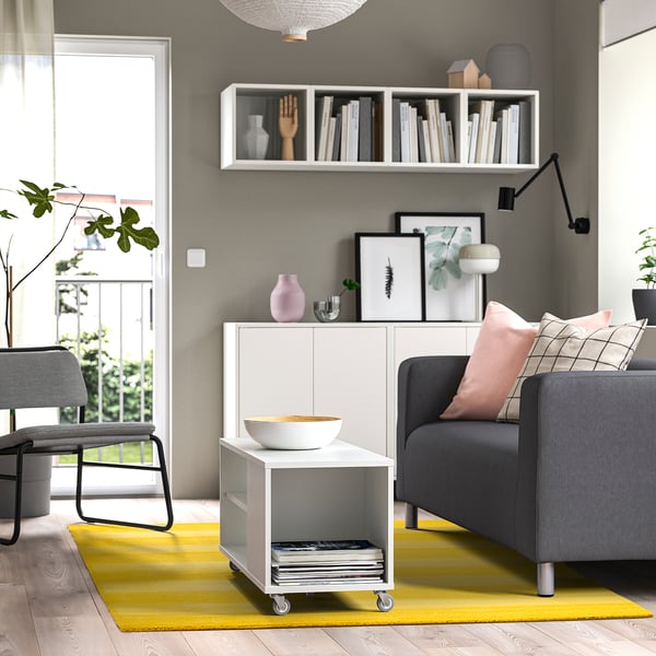 A cosy living room with a LANDSVÄG yellow rug, grey couch, white cabinet, and potted plants.