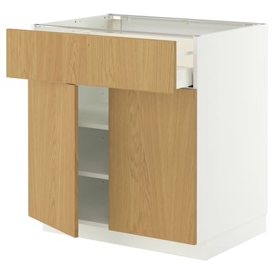 A white METOD kitchen cabinet with wooden doors and drawers, including one open drawer.