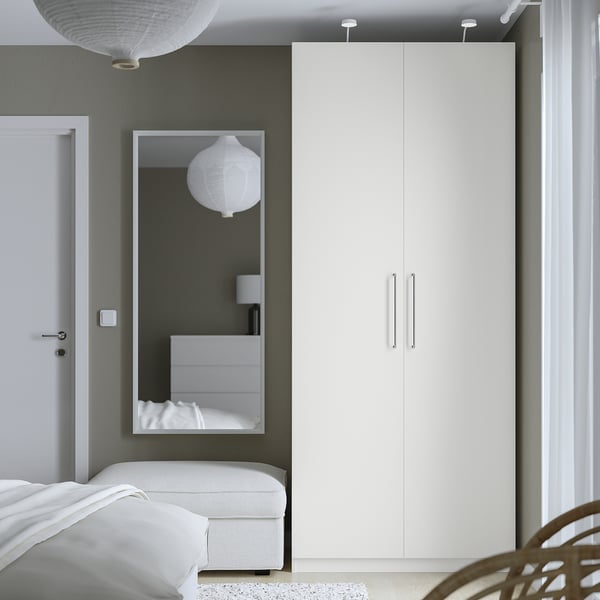 High white PAX wardrobe with mirror beside bed, soft lamp light.