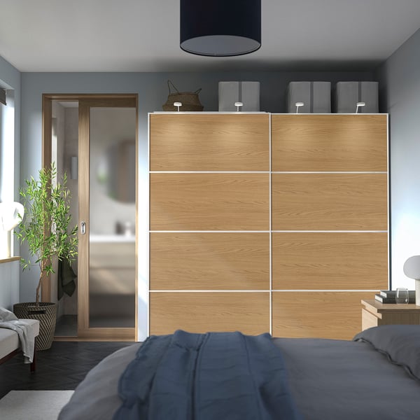 Modern bedroom with light oak PAX wardrobe, dark blue bedding, and corner plant.