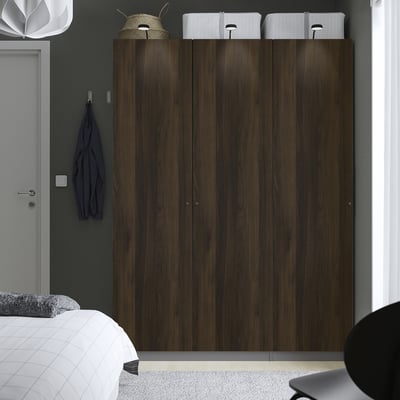 Modern bedroom with large wood PAX wardrobe, white storage, blue towel, grey door, partial white bed with grey pillow, minimalist design.