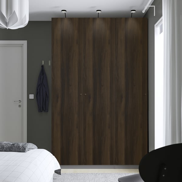 Minimalist bedroom with large dark brown PAX wardrobe, white bed, and grey walls. Blue garment hangs on wall hooks.