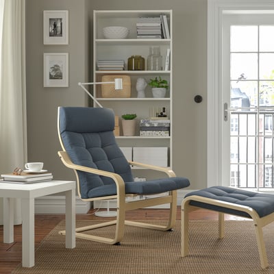 Modern living room with grey POÄNG chair, footstool, side table, bookshelf, large window.