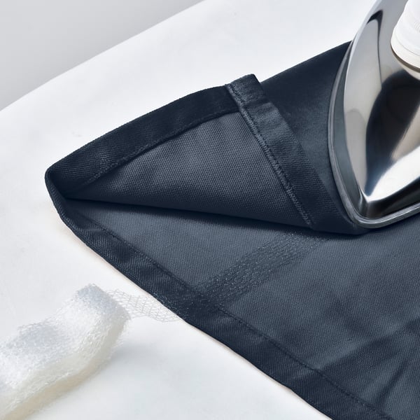 Ironing dark blue velvet curtains, showcasing their thick, luxurious texture and pleated design.