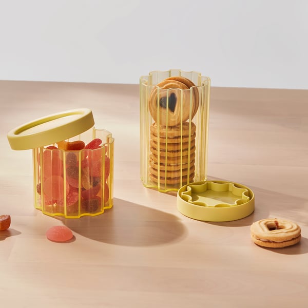 Two transparent jars with yellow lids store cookies and candies, keeping snacks fresh and organised on a wooden surface.
