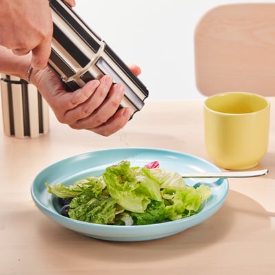 Hand grinding pepper into salad bowl. Modern spice mill grinds fresh spices, avoids residue on table.