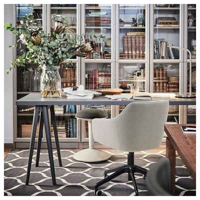 Home office setup with glass bookshelves, grey TOSSBERG chair, desk with green plant, books, and modern decor.