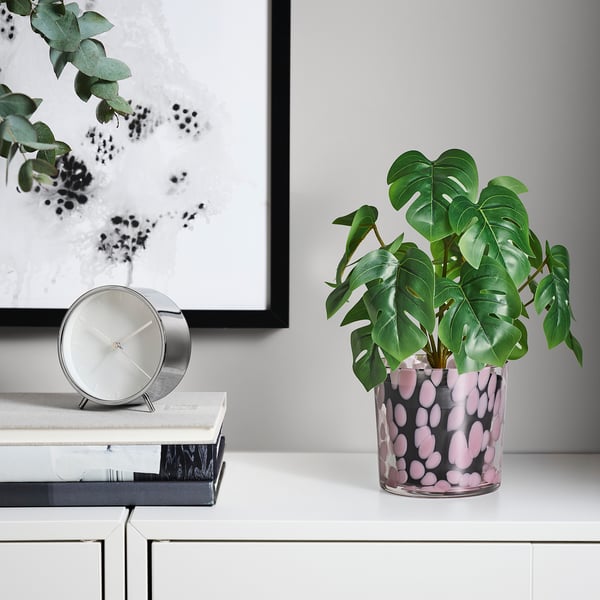 Minimalist desk with glass plant pot, green plant, clock, and wall art.