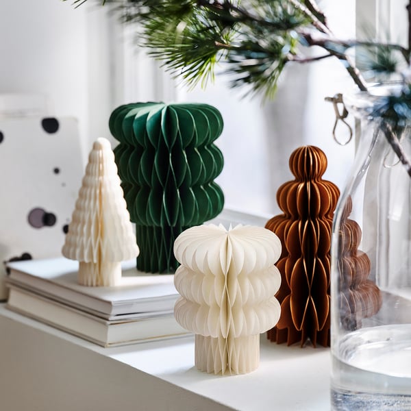 Four colourful paper honeycomb christmas trees in green, white, and brown on a shelf, with one being smaller, creating a festive holiday decoration.