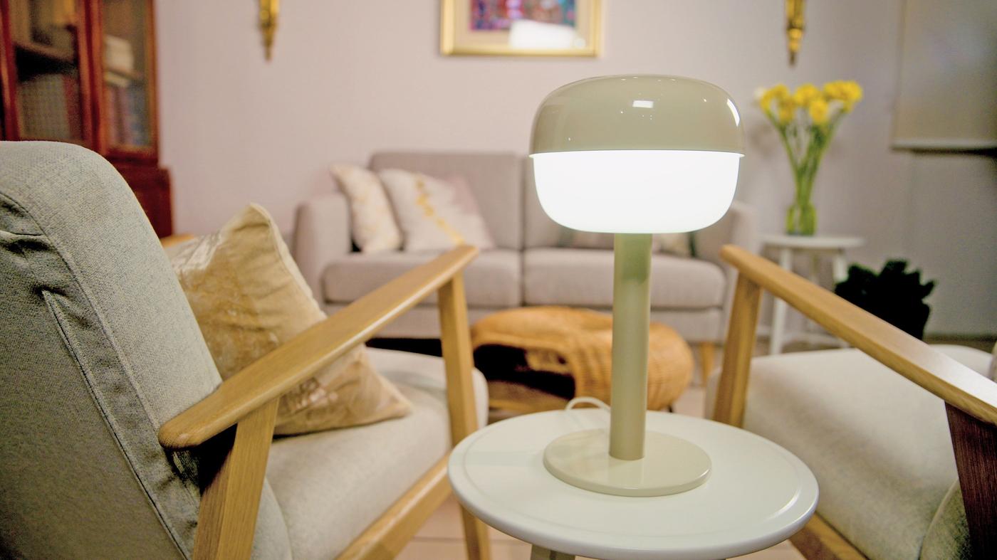 A green illuminated lamp on a table, with chairs to each side and a sofa behind.