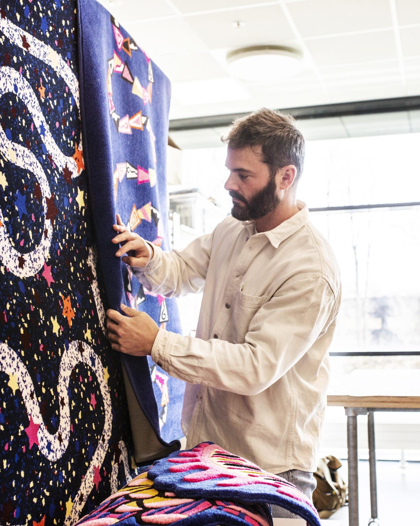 Luis Gomez Barquin looking at two of his rug designs hanging on display.