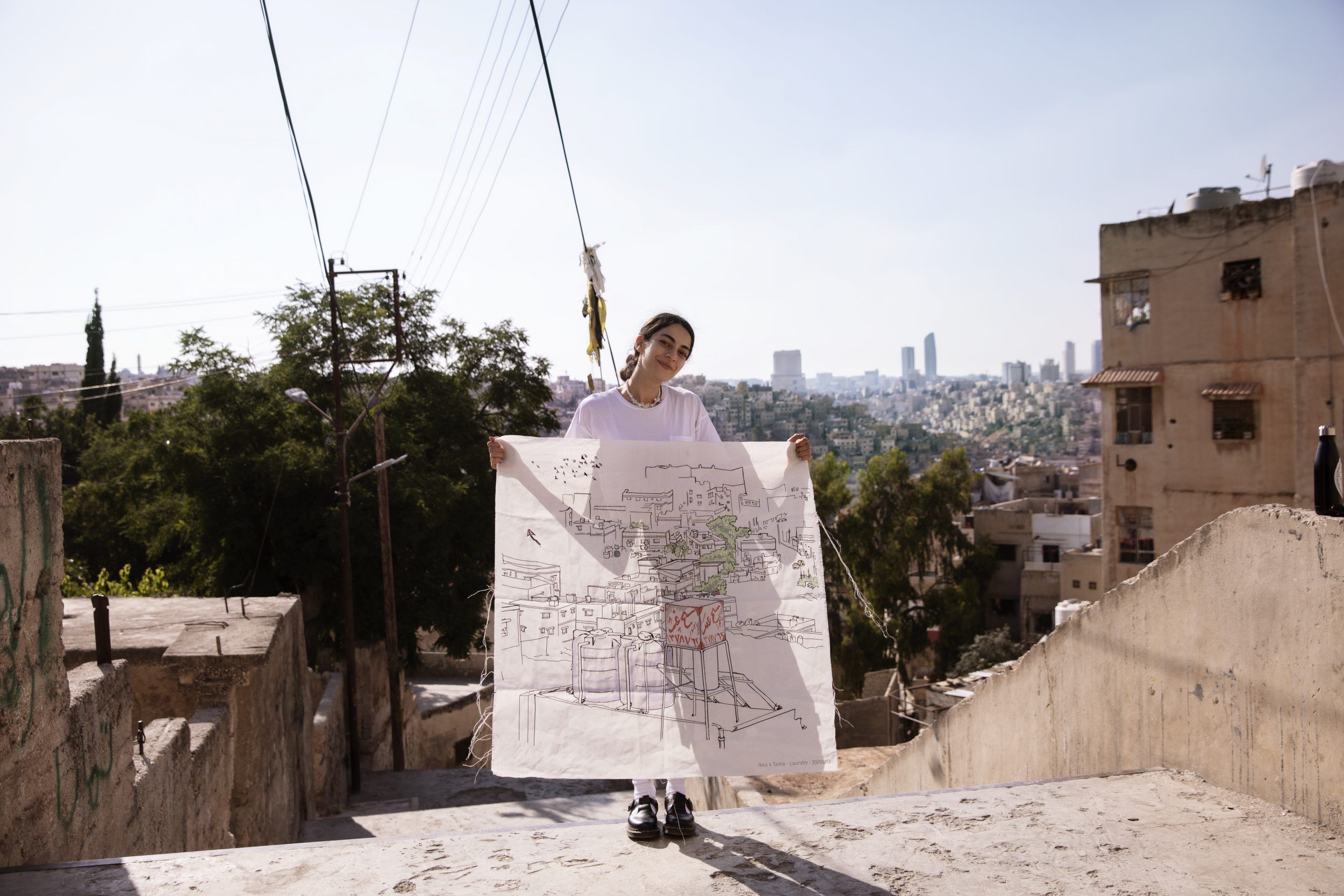 An artisan holding up a piece of white fabric with black embroidery.